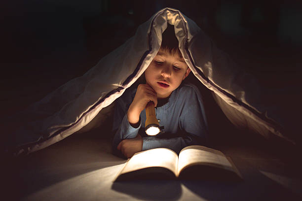 niño leyendo un libro bajo las cubiertas con linterna - child bedtime imagination dark fotografías e imágenes de stock