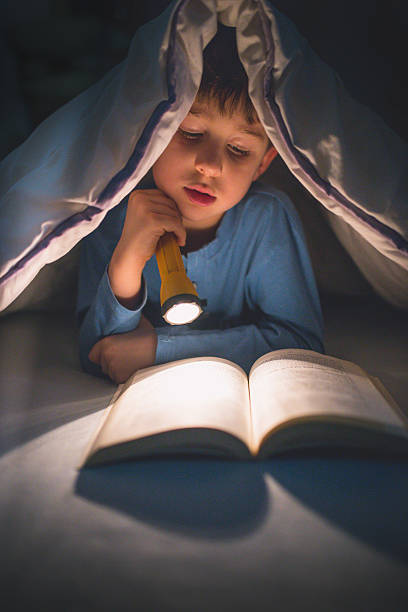 istock Little boy reading a book under the covers with flashlight 639454760