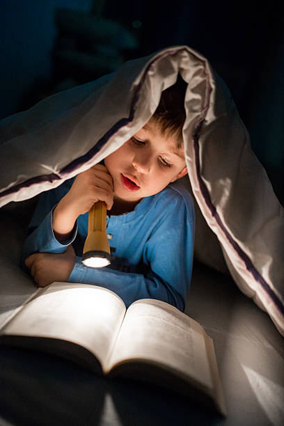 istock Little boy reading a book under the covers with flashlight 639455012