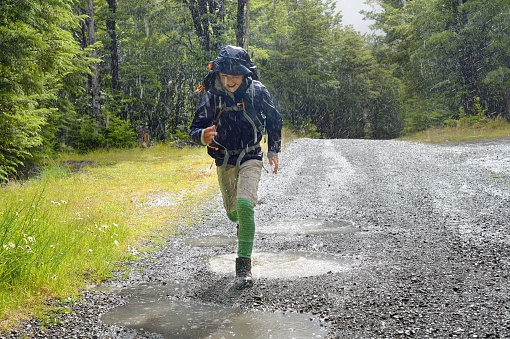 Young New Zealand boy in hiking/tramping clothing, jumping through puddles in the rain.