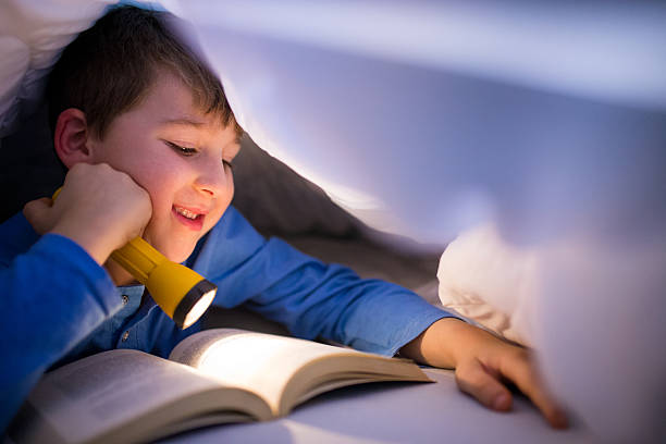 istock Little boy reading a book under the covers with flashlight 639455326