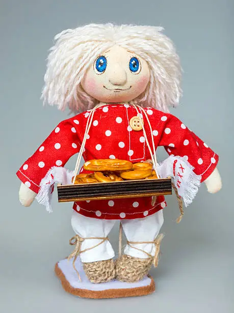 Handmade rag-doll. Studio shooting. Cloth doll boy in red russian shirt. Tray with a bread-rings on his neck. The russian doll standing on gray background