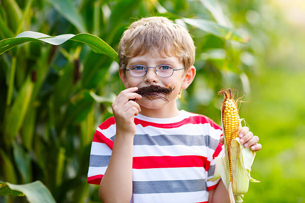 Kid boy with sweet corn having fun with moustache