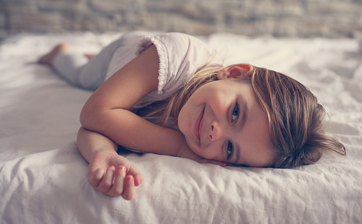 a girl child sleeps on a bed at home on a white cotton bed and smiles sweetly in her sleep with her hands folded under her cheeks