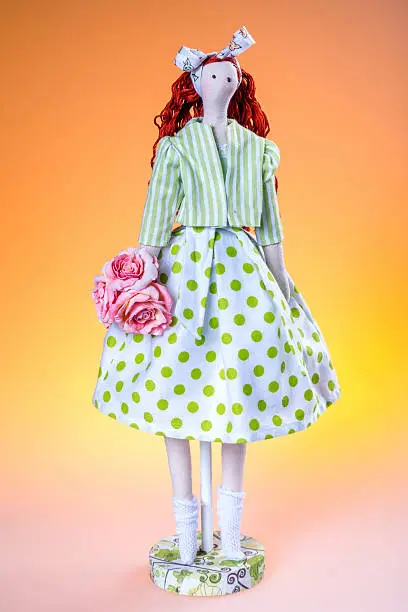 Handmade rag-doll. Studio shooting. Cloth doll girl in polka-dot dress and in jacket with stripes. Tilda doll standing on colorful background