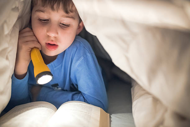 istock Little boy reading a book under the covers with flashlight 639460864