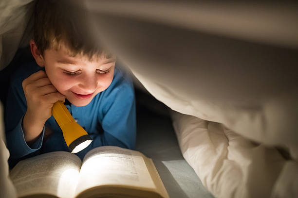 istock Little boy reading a book under the covers with flashlight 639461022