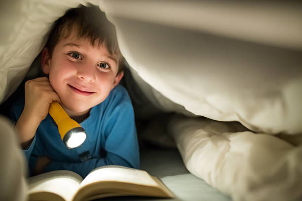 istock Little boy reading a book under the covers with flashlight 639461096