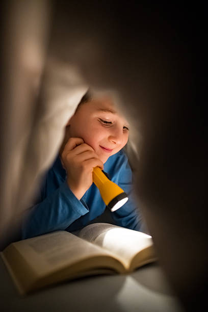 istock Little boy reading a book under the covers with flashlight 639461170