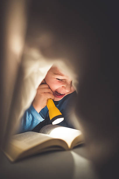 istock Little boy reading a book under the covers with flashlight 639461340