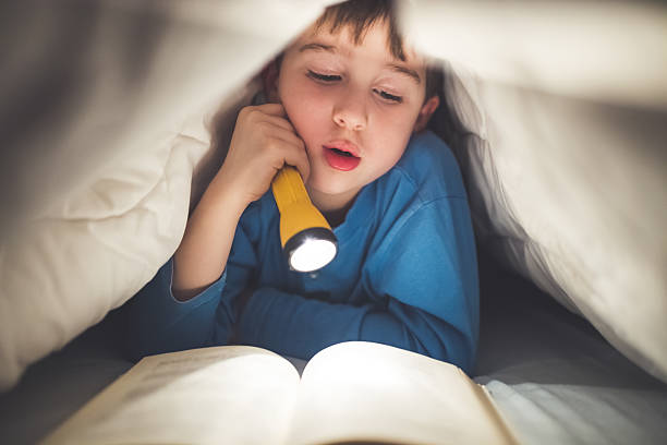 istock Little boy reading a book under the covers with flashlight 639461404