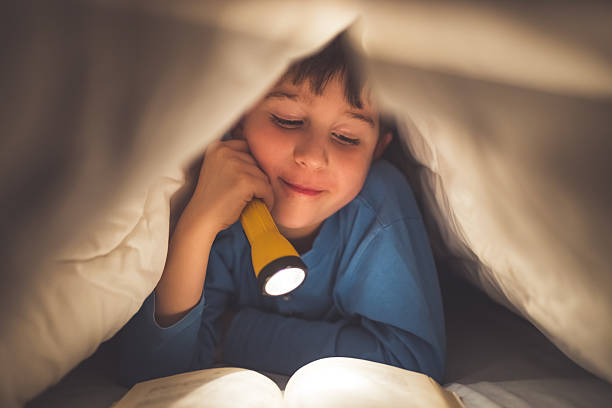 istock Little boy reading a book under the covers with flashlight 639461474