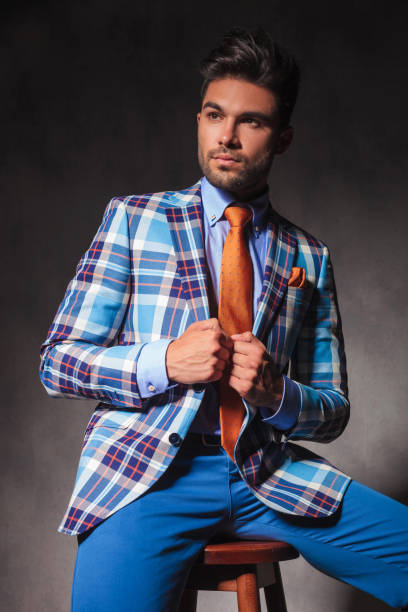 istock seated young man in checkered suit holding his collar 639461562
