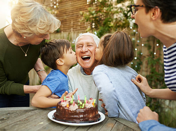 Kisses for the birthday boy Shot of a happy family celebrating a birthday together outside mature men photos stock pictures, royalty-free photos & images