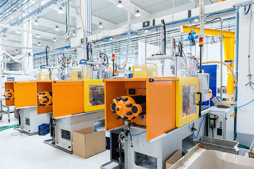 Horizontal image of huge new modern factory with robots and machines producing industrial plastic pieces and equipment. Wide angle view of futuristic machines placed on flooring, arranged in a row. Wide angle view, no people, space for copy.