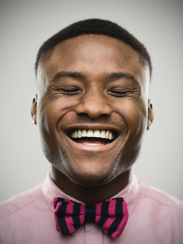 Close-up of cheerful man. Happy male is with eyes closed against gray background. He is wearing pink bow tie. Vertical studio photography from a DSLR camera. Sharp focus on eyes.
