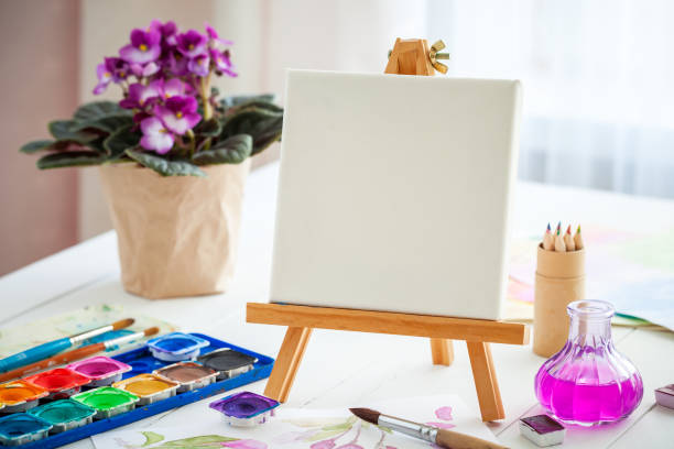 istock Watercolor paints, brushes , canvas on easel and violet flower 639481876