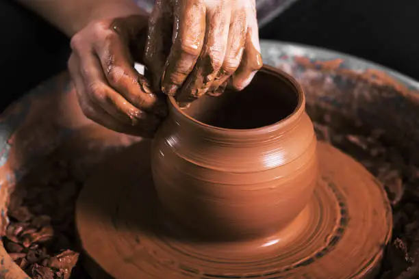 Photo of hands of a potter, creating an earthen jar
