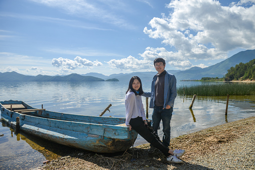 Young Asian couple looking at camera on lake bank, shot at Lugu Lake, Lijiang, Yunnan, China
