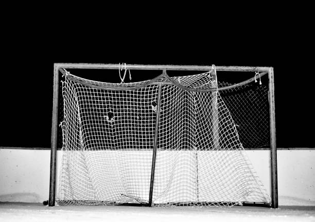 Close-up of tattered and frayed mesh on a hockey net on an outdoor ice skating rink at night in black and white