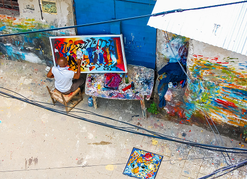 Stone Town, Zanzibar, Tanzania - September 23, 2010: Local African artist works on colorful African paintings in outdoor workshop in Stone Town