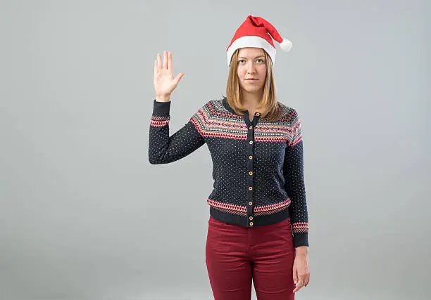Pretty woman wearing Santa hat showing Vulcan greeting isolated on gray