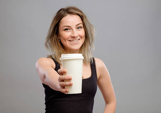 Young woman giving hot coffee to camera
