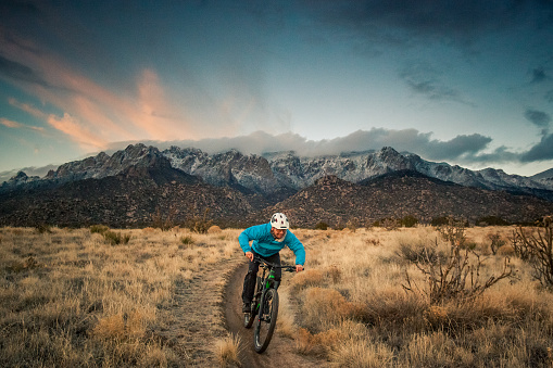 happy and joyful smiling mountain biking man descending desert mountain terrain in the cool blue hues of dusk.  wide angle horizontal composition.  sandia mountains.  albuquerque, new mexico.