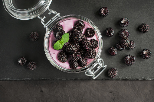 Yogurt with black raspberry or blackberry in glass jar on black slate board