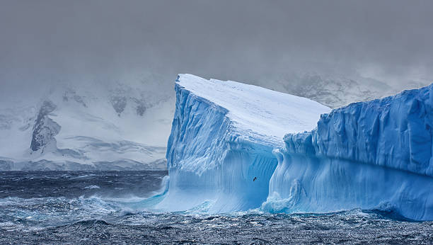 Massive Iceberg floating in Antarctica Massive Iceberg floating in the Southern Ocean in Antarctica with snow covered mountains in the background iceberg ice formation photos stock pictures, royalty-free photos & images