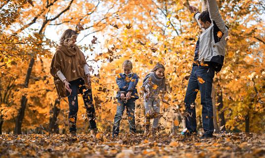 Happy family having fun in autumn day at the park while throwing leaves.