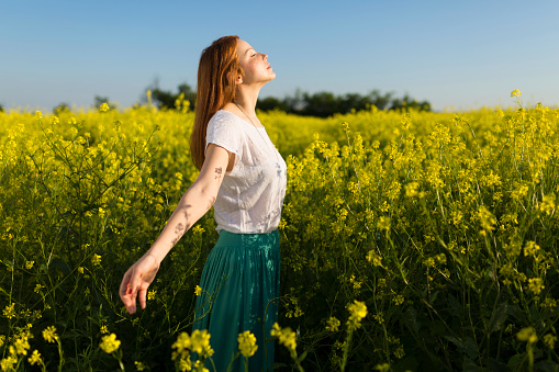 Beautiful redhead enjoying a carefree summer day in the middle of a yellow flower field.