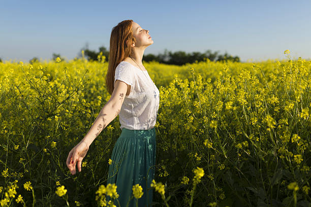 Left daydreaming Beautiful redhead enjoying a carefree summer day in the middle of a yellow flower field. scene scented stock pictures, royalty-free photos & images