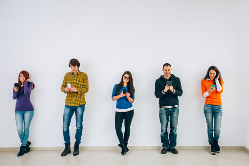 Group of people texting in a row in front of big empty white wall, with copy space.