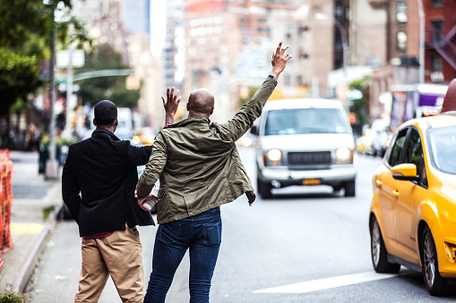 Young gay couple hailing to taxis on the streets in Greenwich Village, New York.