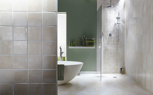 The interior of a simple, modern bathroom in a cool, green tone. There is a bath, shower, a bath towel . There are light grey tiles in the shower with running water
