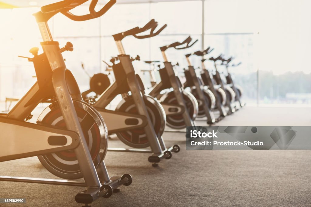 Modern gym interior with equipment, fitness exercise bikes Modern gym interior with equipment. Fitness club with row of training exercise bikes in evening backlight. Healthy lifestyle concept Gym Stock Photo