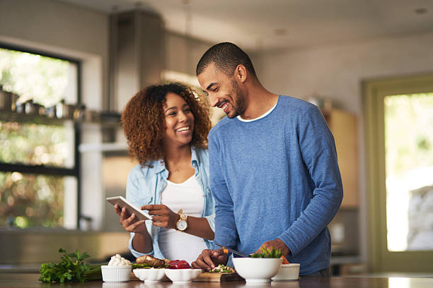 Our food looks just as good as the recipe Shot of a happy young couple using a digital tablet while preparing a healthy meal together at home paleo diet stock pictures, royalty-free photos & images
