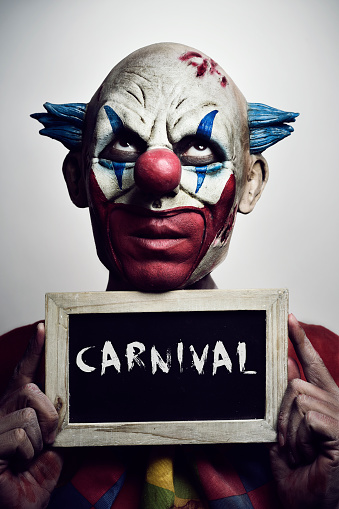 portrait of a scary evil clown with a chalkboard with the word carnival written in it