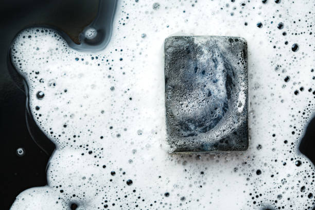 istock Black coal bar of soap in foam on dark 639598562
