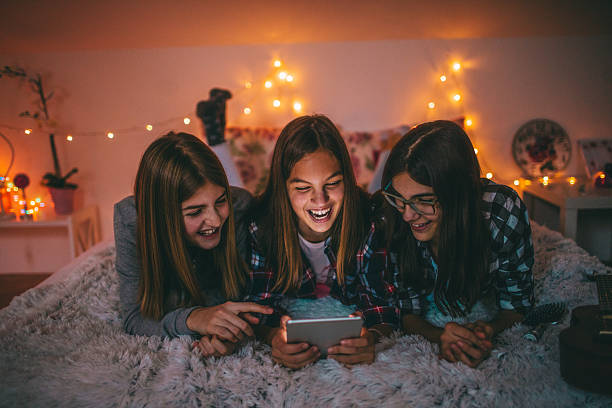 Teenagers and social networking Photo of young teenagers hanging together, in one of the girls bedroom, spending time on social networks slumber party stock pictures, royalty-free photos & images