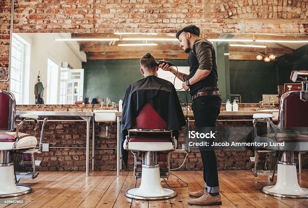 Hairstylist serving client at barber shop Rear view shot of handsome hairdresser cutting hair of male client. Hairstylist serving client at barber shop. Barber Shop Stock Photo