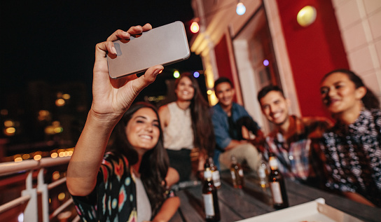 Friends having a party on the rooftop making a selfie with smart phone. Young people taking self portrait during party.