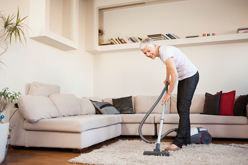 Woman cleaning carpet with a vacuum cleaner in room