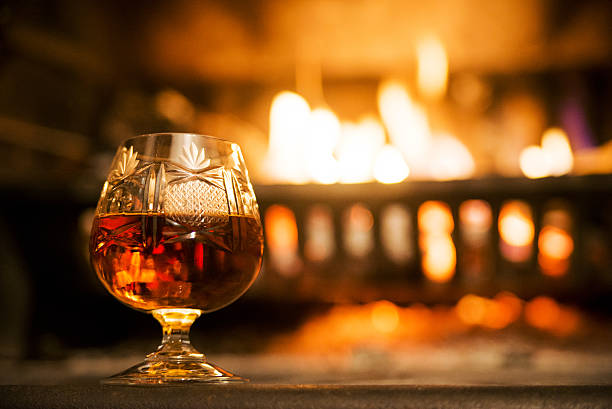 bicchiere di liquore duro di fronte alla notte camino - brandy foto e immagini stock