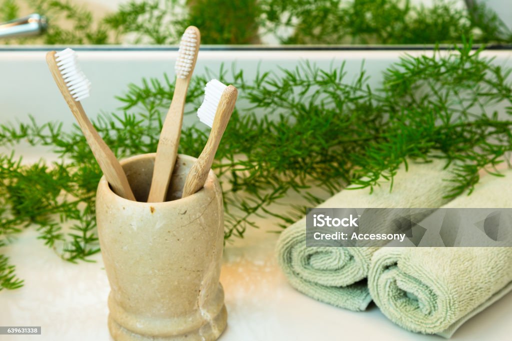 Bambus-Zahnbürsten in Tasse, Handtücher und Grüns auf Badezimmer-Arbeitsplatte - Lizenzfrei Zahnbürste Stock-Foto