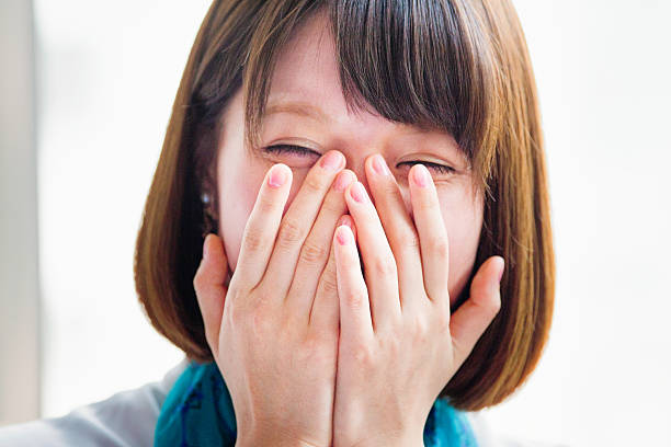 Young Japanese woman hiding her face while laughing.