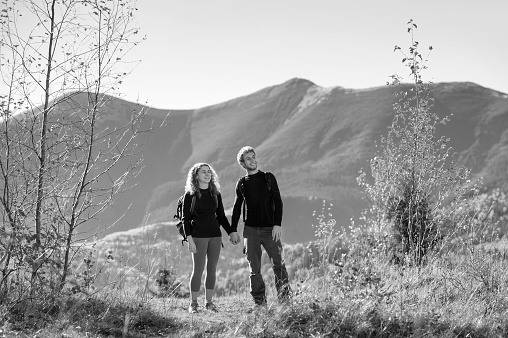 Young happy couple tourists holding hands smiling and looking into distance on a warm sunny day in the mountains. Mountain on the background. black and white