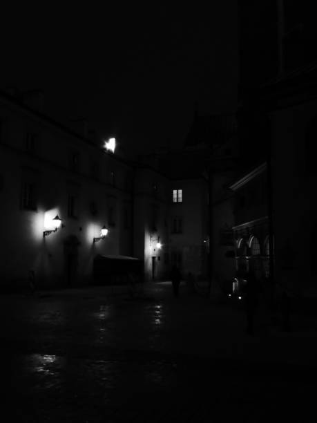 Lone walker barely seen on a dark night in Krakow. Courtway lit by three lamps reflected on the street.