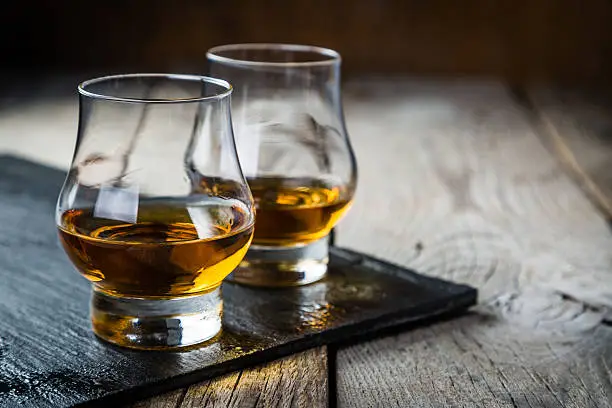 Whiskey with ice in glasses, rustic wood background, copy space